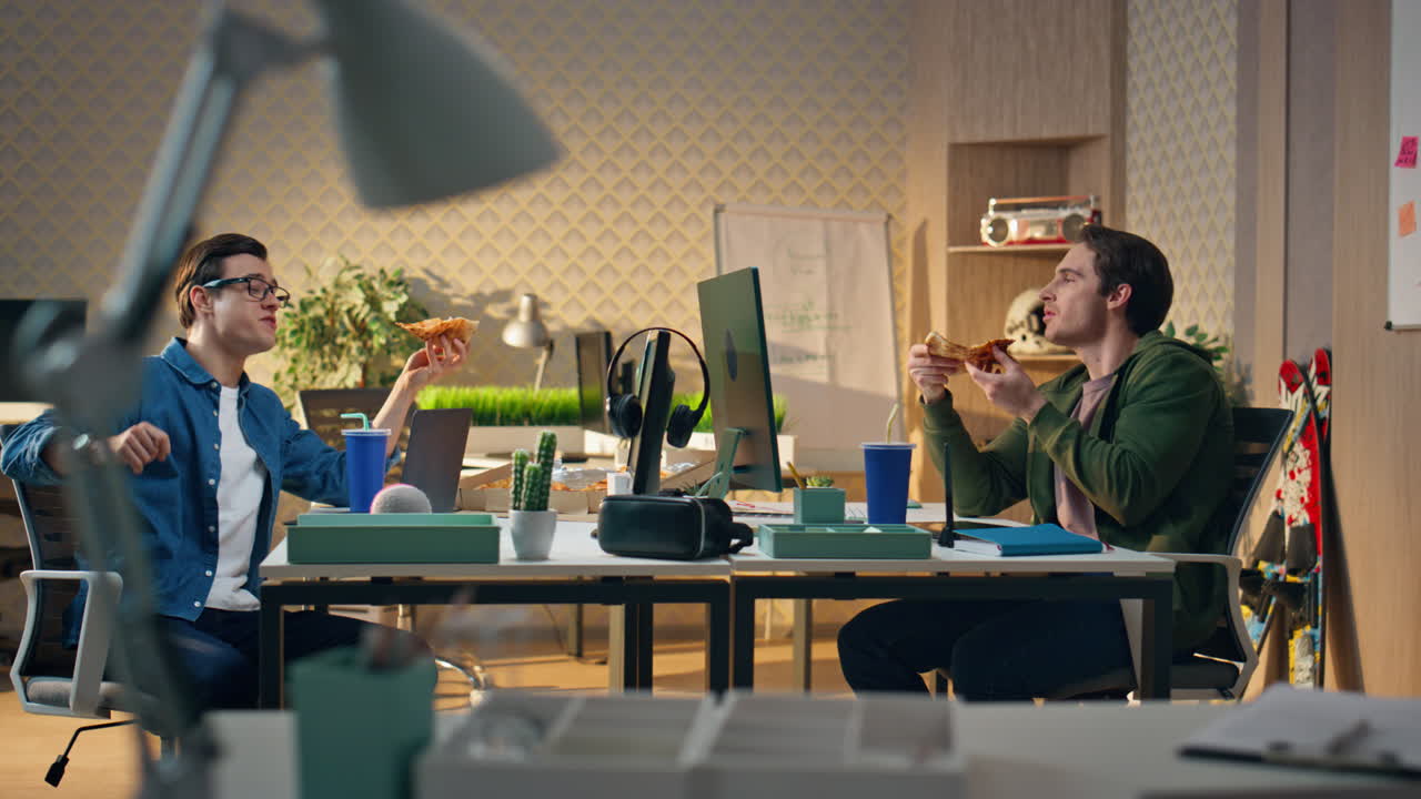 lavoratori d'ufficio che mangiano il pranzo monitorano il tavolo dell'ufficio. ragazzi sorridenti che parlano insieme