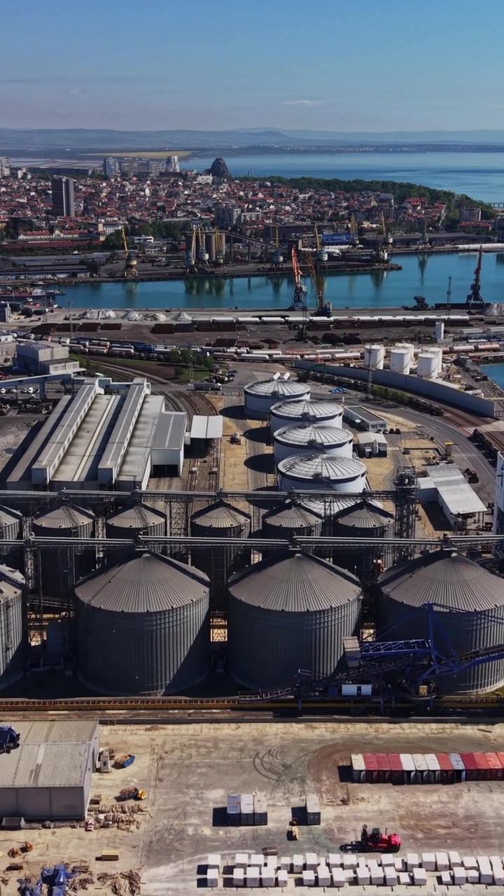 Operações de carga em porto industrial com silos e atividade de transporte marítimo.