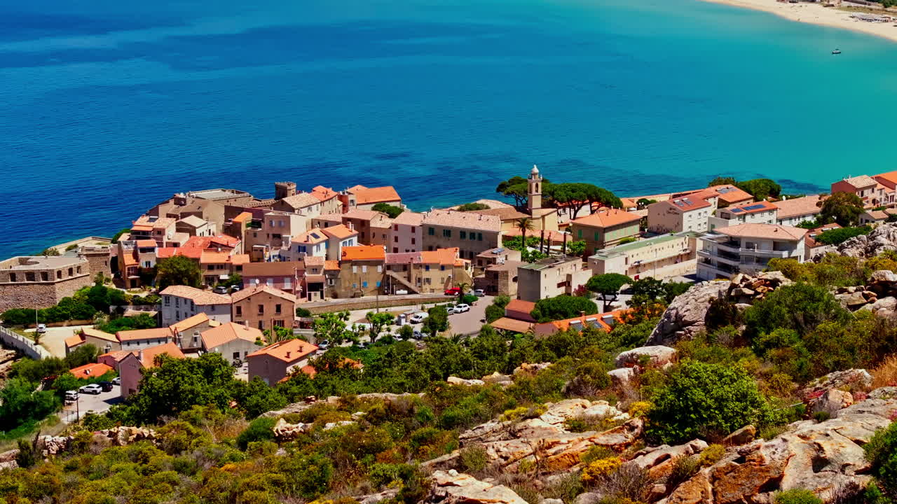 Aerial drone shot over the coastal town of Algajola in Balagne, Corsica, France. High view of the local town and the turquoise sea. Bright blue sky. Summer holidays destination