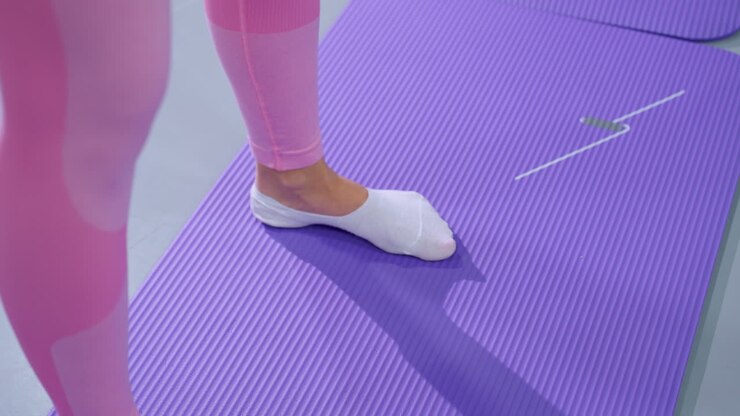 Leg view of a woman in pink balancing on a purple mat during a workout session, she wears white socks while focusing on stability and strength training in a well-lit gym setting