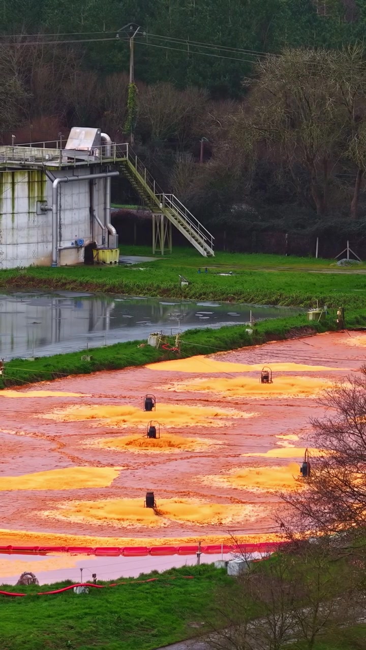 Vista verticale di un impianto di trattamento delle acque reflue con un bacino di sedimentazione del ferro di colore arancione brillante e attrezzature di aerazione vicino a un edificio industriale a Jelgava, Lettonia.