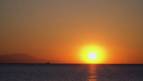 beautiful static shot of a sunrise with boat and mountains on horizon