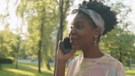 cheerful african american  woman walking in park and speaking on phone