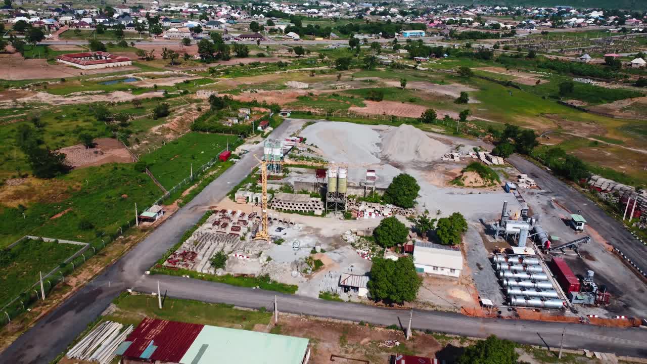Drone video captures a bustling industrial site surrounded by green fields under bright daylight. Equipment and storage piles are visible, highlighting construction activity in countryside, Africa