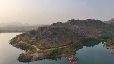 Aerial---Scenic-wide-shot-of-a-rocky-outcrop-surrounded-by-a-lake-at-sunset