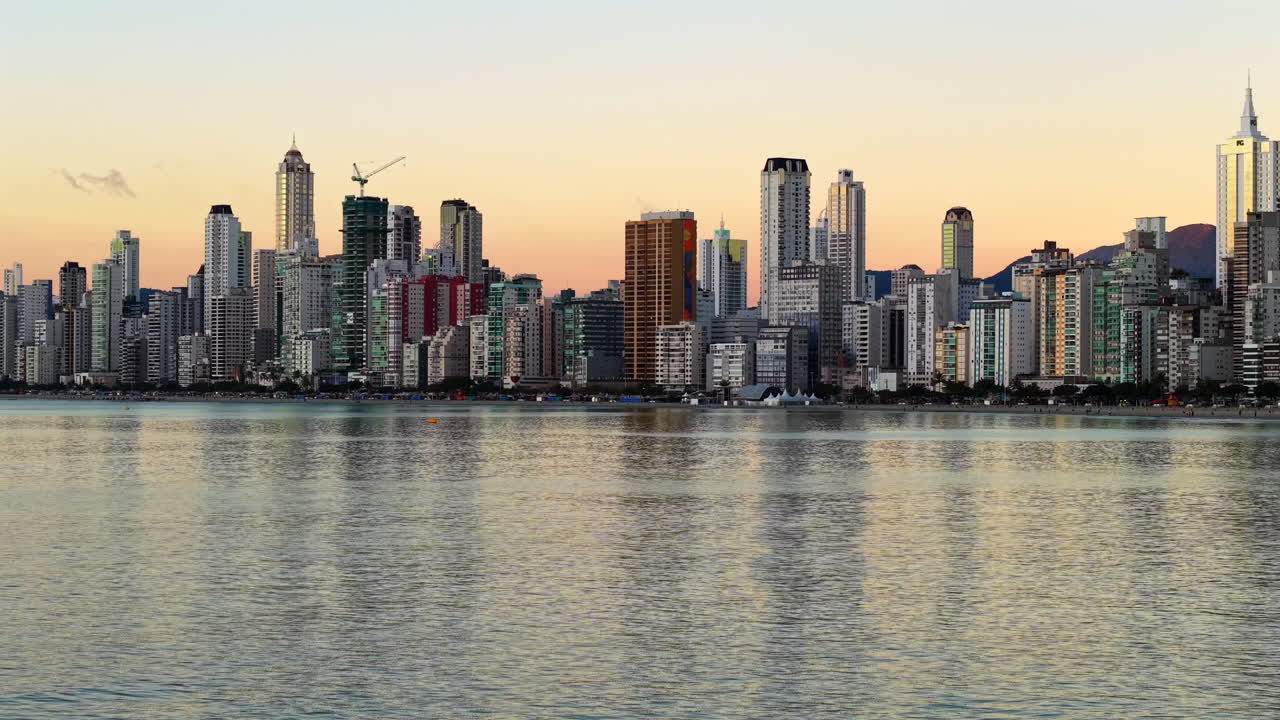 Aerial drone fly Balneario Camboriu, Santa Catarina beach town with sunrise skyline, above reflecting water