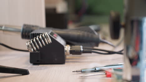 a close-up view of a technician's gloved hand dropping a soldering iron in an electronics workshop, with various tools in the background