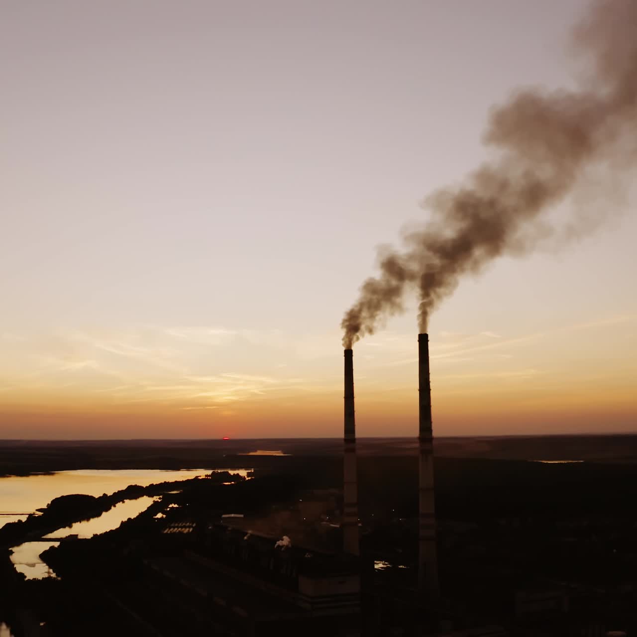 Manufacturing near the river at darkness. Two pipes with dirty smoke going into the air on the nature background in the evening.