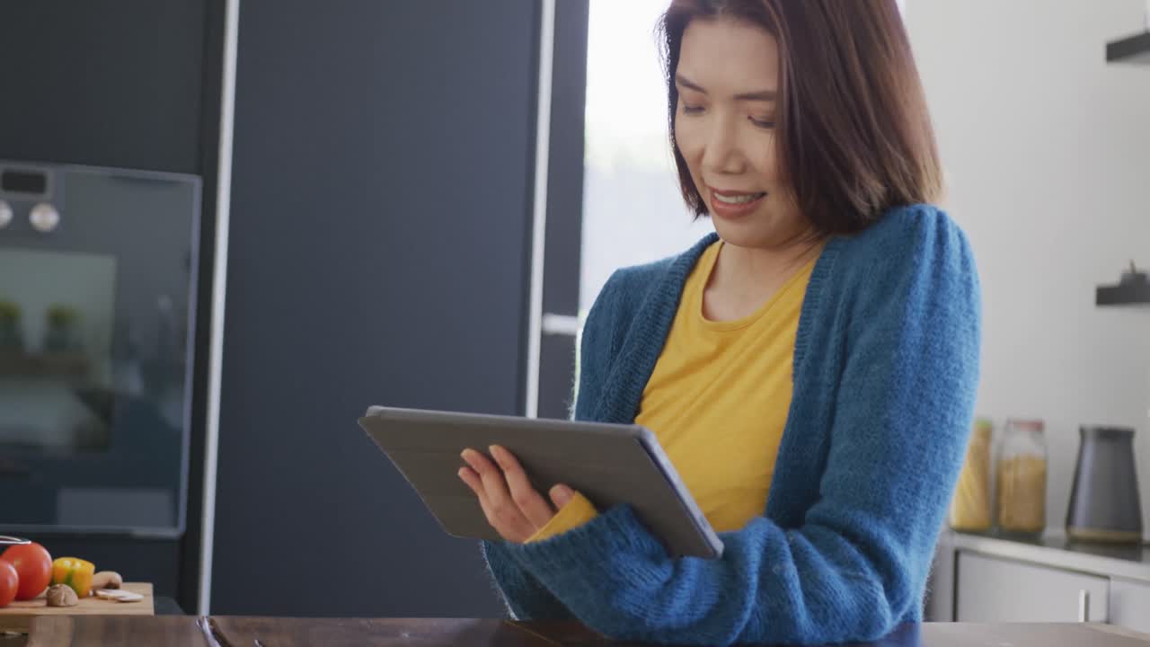 Video of happy diverse couple preparing food using recipe on tablet in kitchen at home