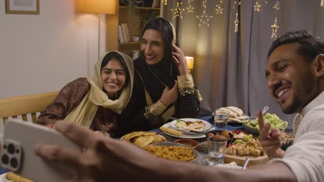 familia musulmana sentada alrededor de una mesa en casa con comida para comer celebrando eid posando para selfie