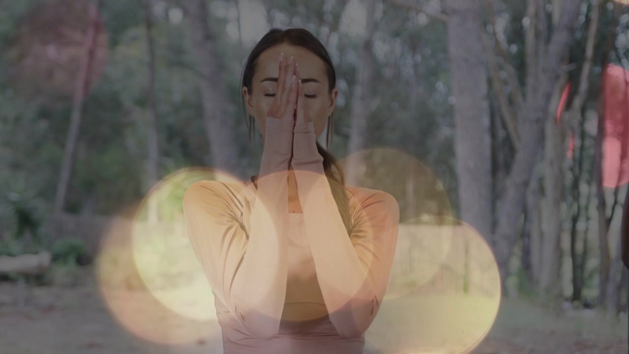 Mujer realizando un flujo de meditación en el bosque, con superposiciones de bokeh que inician las manos uniéndose en oración