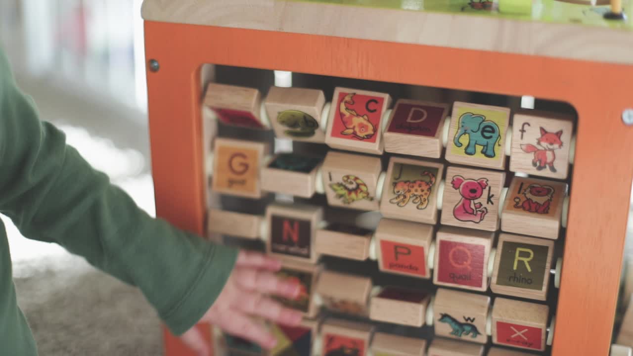 Slow motion shot of baby's hand spinning alphabet squares on a wooden toy.