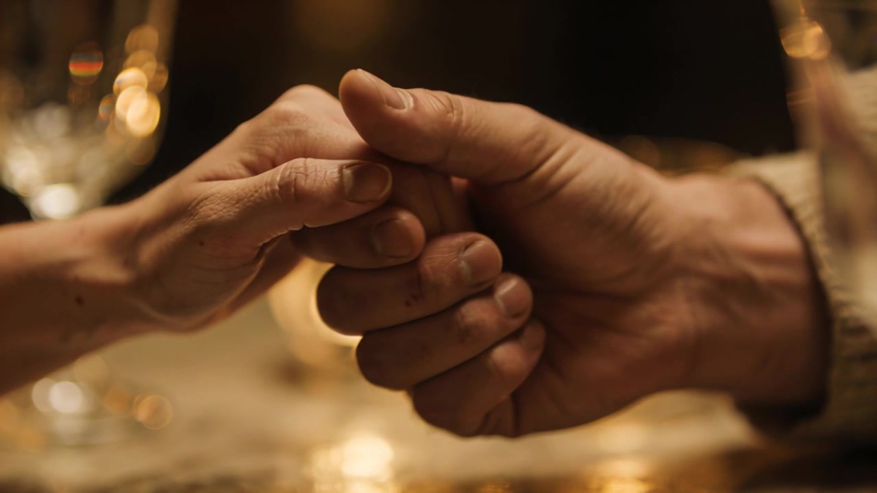 Una mano piccola che si stringe in una mano grande al tavolo, la presa che offre sostegno, occhiali, manica a maglia.
