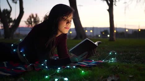 una linda mujer joven que lee un libro de cuentos de ficción al aire libre al atardecer con luces brillantes que se deslizan hacia la derecha