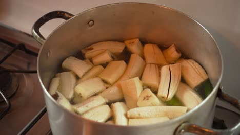 chunks of green plantain cooking in boiling water inside a large silver pot on stovetop. latin american cuisine. ideal for food content, recipes, or kitchen footage.