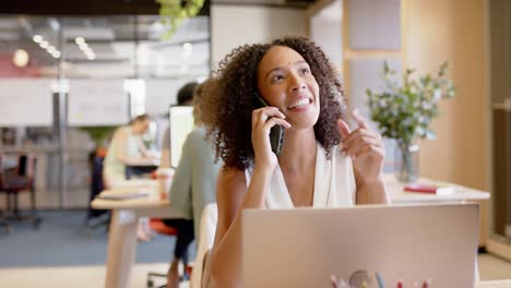 Biracial-Geschäftsfrau,-Die-Im-Büro-Auf-Dem-Smartphone-Spricht-Und-Einen-Laptop-Benutzt,-In-Zeitlupe