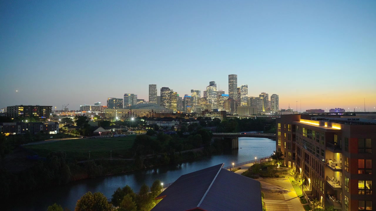 Weitwinkelansicht zur blauen Stunde der Skyline von Downtown Houston mit Blick auf den Buffalo Bayou, mit dem sich schlängelnden Fluss im Vordergrund und beleuchteten Wolkenkratzern in der Abenddämmerung in Houston, Texas, USA.