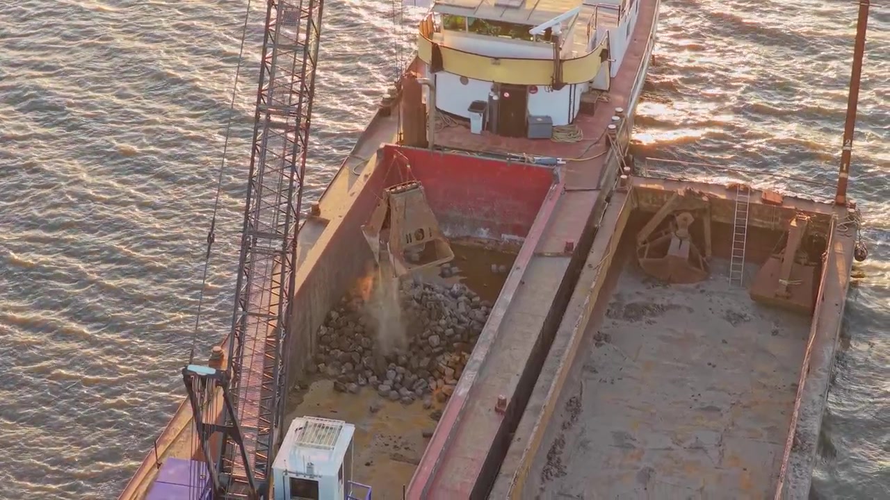Gru che carica rocce su una chiatta in un fiume.