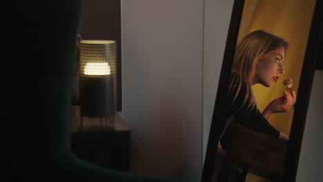 woman applying makeup in front of a mirror at night
