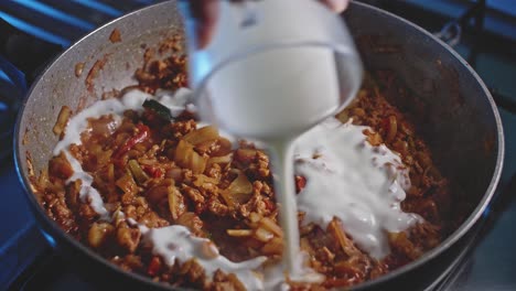 Pouring-sauces,-cream-and-tomatoes-into-a-wok-with-meat-and-vegetables-for-homemade-mexican-food,-close-up-view