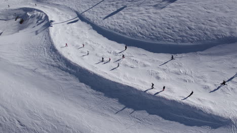 group of amateur skier skiing downhill snowy slope during sunny day in winter - aerial top down