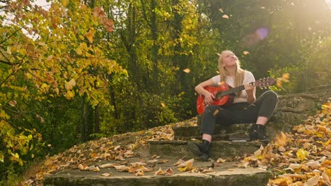 happy woman plays guitar autumn fall gold leaves woodland sun rays