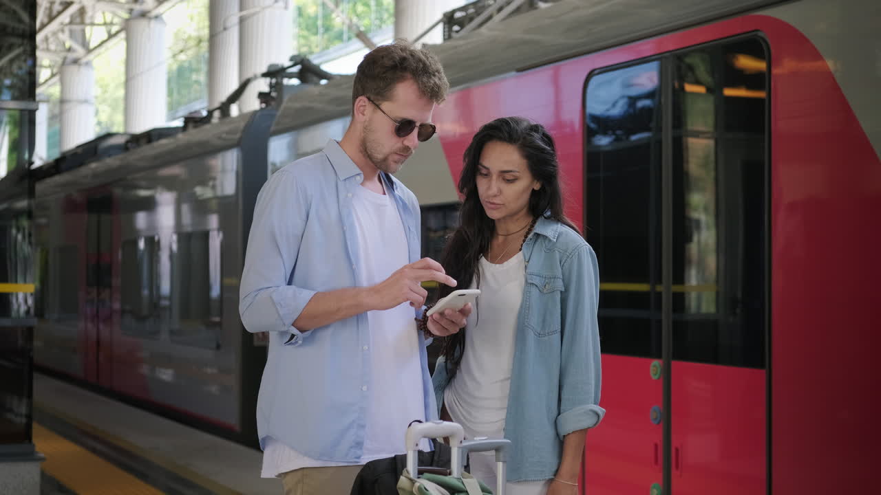 Pareja en la estación de tren revisando el teléfono móvil