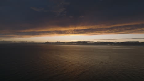 drone shot flying over the tasman bay ocean towards the mountains in the distance during sunrise. new zealand