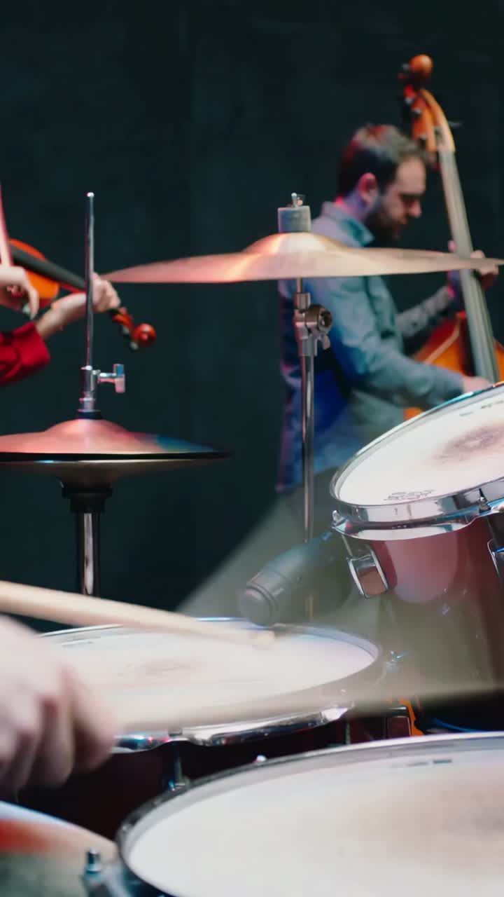 Video verticale: batterista che colpisce le bacchette iniziando velocemente a suonare la batteria, violinista che suona con l'archetto con una manica rossa