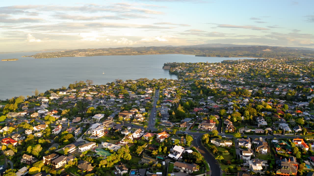 Aerial view of a coastal residential suburb with houses and green trees overlooking a bay