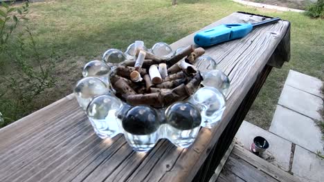 un cenicero lleno de colillas de cigarrillos sentado en una barandilla de madera fuera de una casa en el patio delantero durante el día