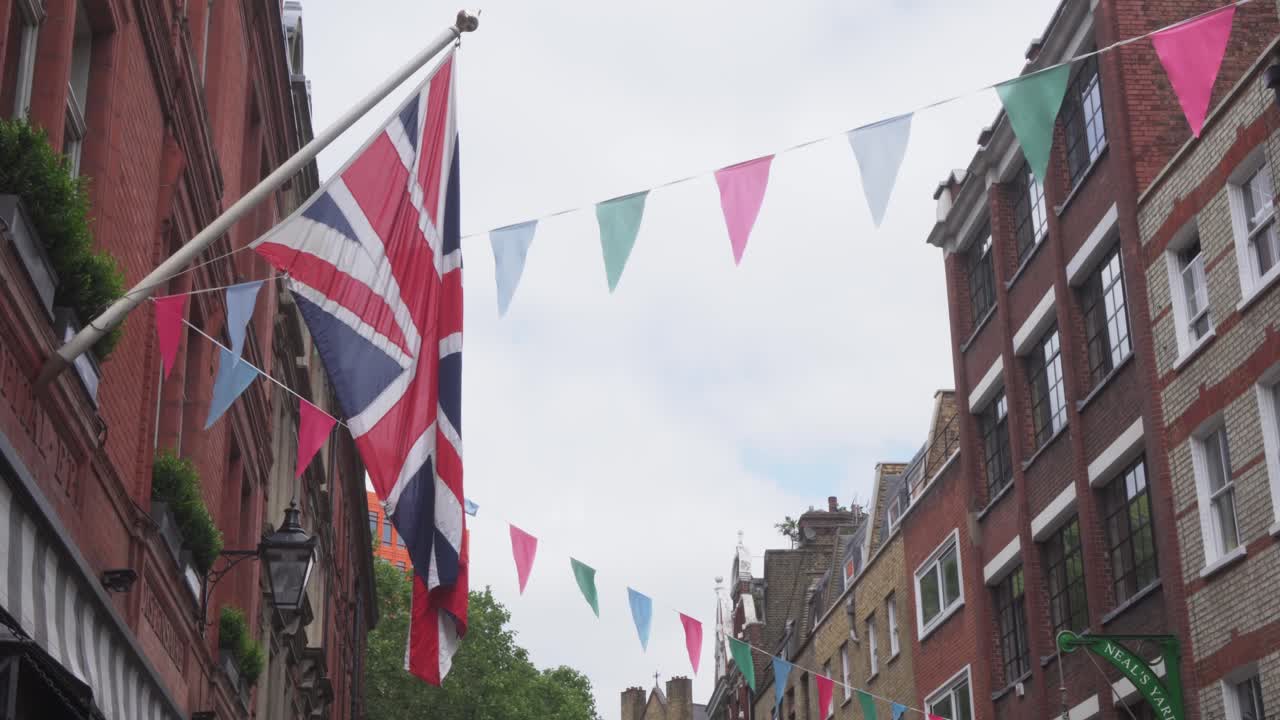 United Kingdom flag hanging on flagpole in London street, colorful triangle flags around, low angle view