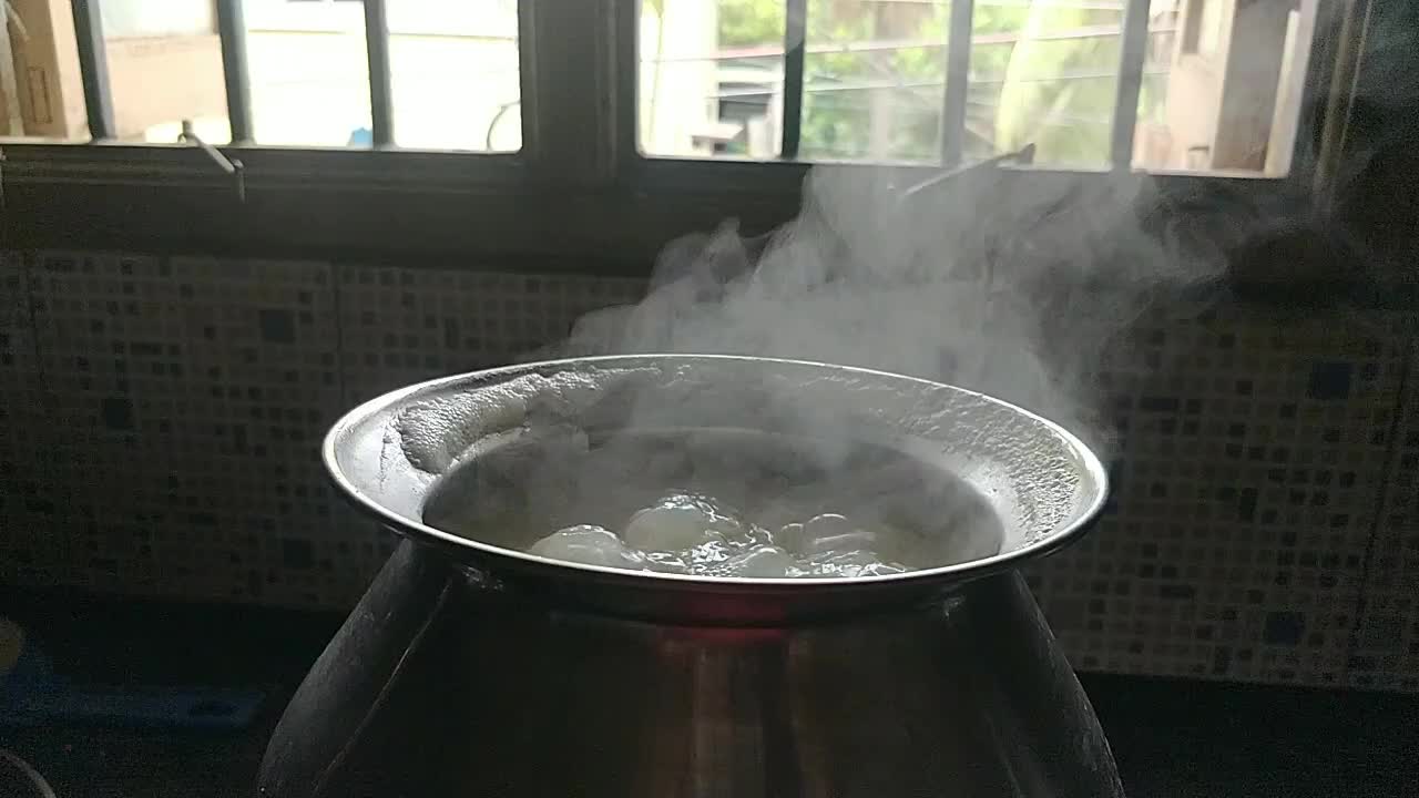 Pot cooking rice in a traditional way by boiling water in a black background with white smoke coming in slow motion