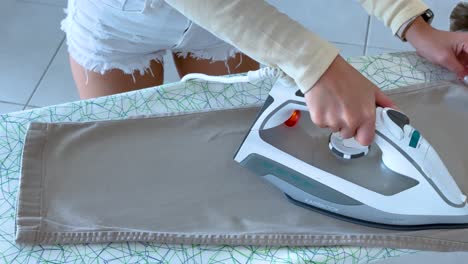 a person irons pants on a patterned board in bright lighting, showcasing domestic chores in a modern setting