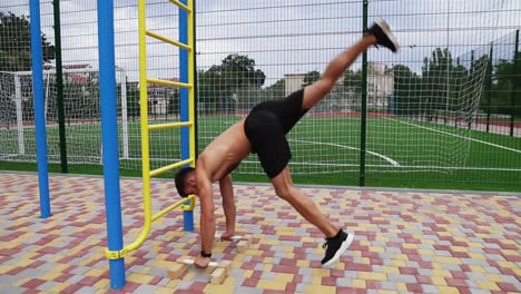 The-young-athlete-is-doing-pushups-on-hands-standing-upside-down-near-the-ladder.-Young-man-topless-in-black-shorts