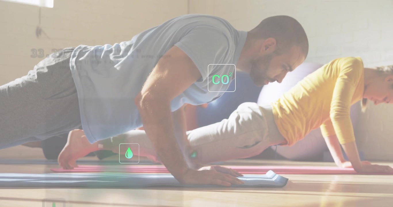 Compañeros de entrenamiento desenrollando colchonetas en el gimnasio, mostrando una etiqueta de CO2 de RA actualizándose mientras sincronizan el ejercicio de plancha a flexión.