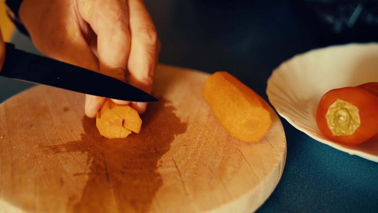 Close-up of hands chopping a fresh carrot on a wooden cutting board. Authentic home cooking footage for food, recipe and healthy lifestyle projects