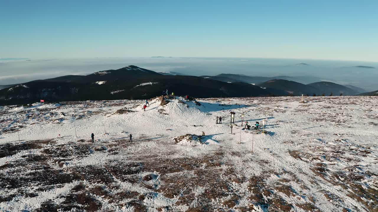 People hiking on top of czech mountain covered with snow from drone