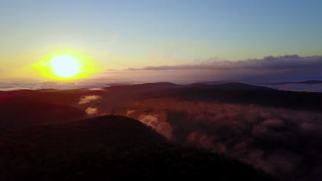 Drone-footage-of-spectacular-sunrise-over-dense-forest-covered-in-broken-fog