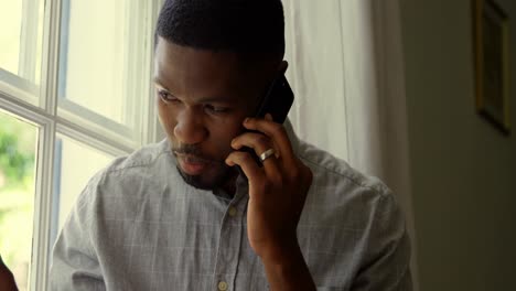 Front-view-of-young-black-man-talking-on-mobile-phone-in-a-comfortable-home-4k