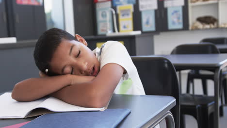 in school, in the classroom, a young biracial student is yawning at his desk with copy space