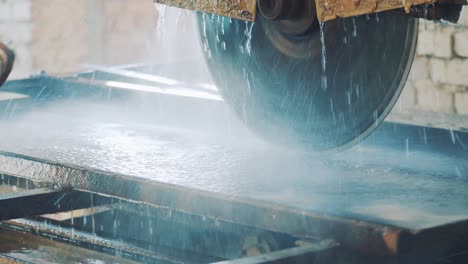 sharp saw blade of modern granite manufacturing equipment prepares to cut stone. saw blade equipment sprays water on granite rock for cooling. saw blade for hard mineral cutting. processing equipment