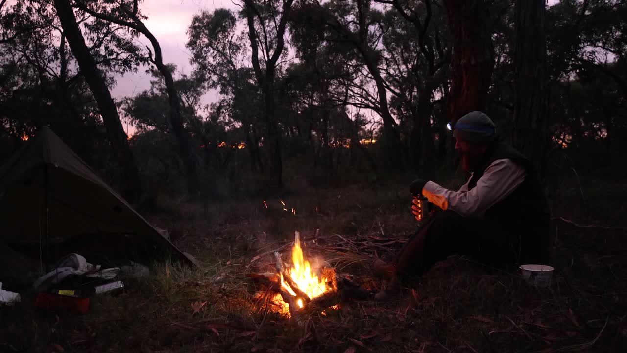 un bosquimano se sienta alrededor de una fogata en el atardecer brilla en el bosque australiano