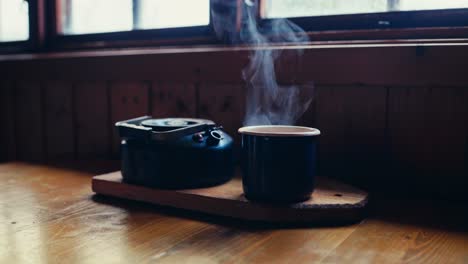 a mug of hot beverage next to a kettle. close-up shot