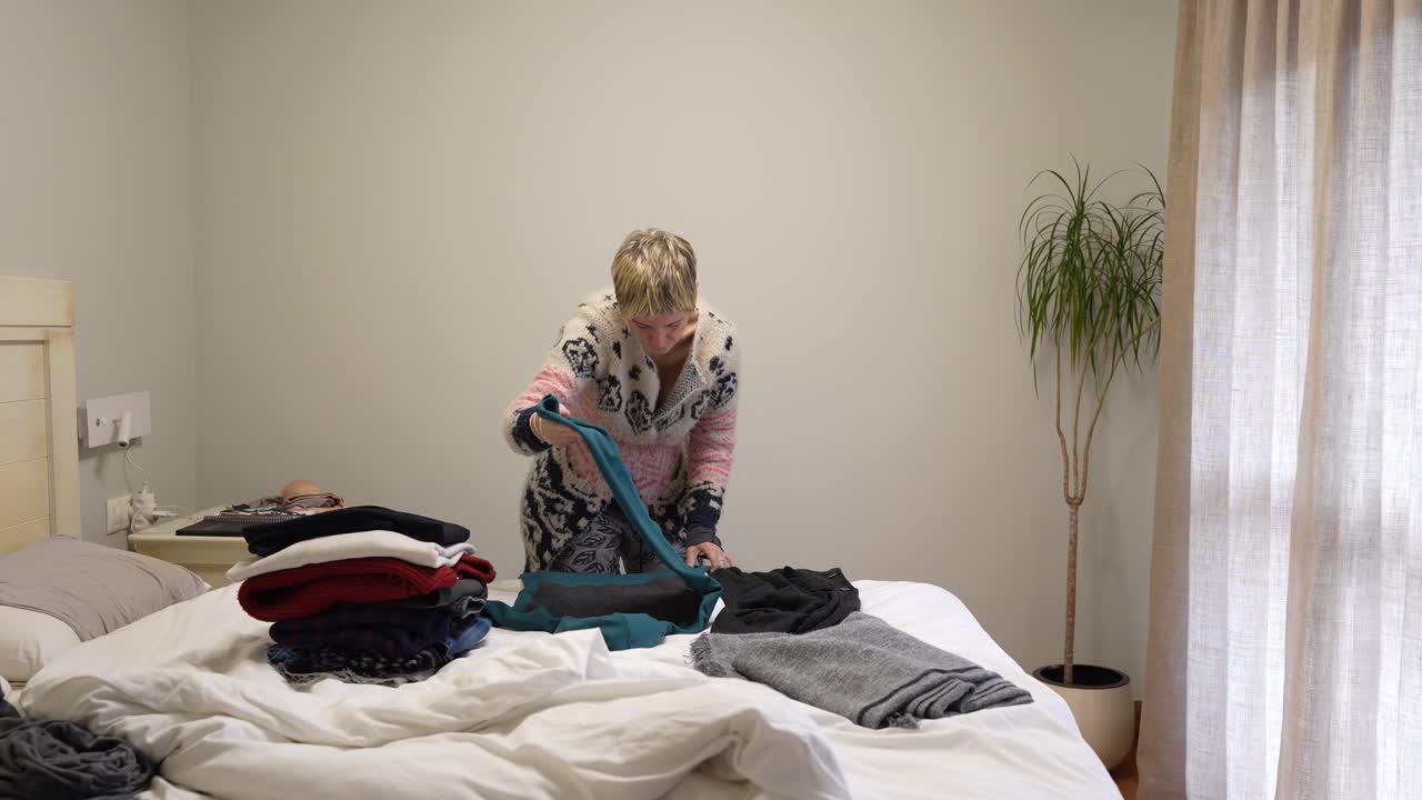 Woman folding clothes on bed in bedroom