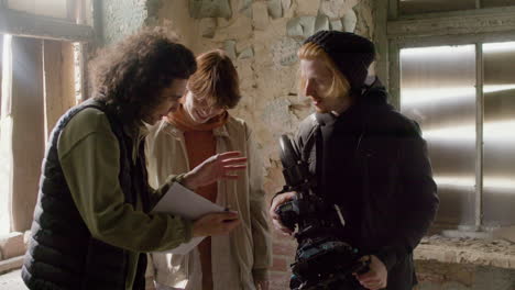 a production worker and cameraman helping his female coworker read a script in a ruined building