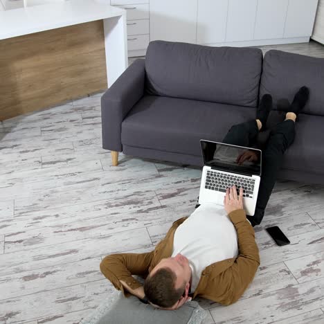 man lying in living room. young man using laptop while lying on floor at home