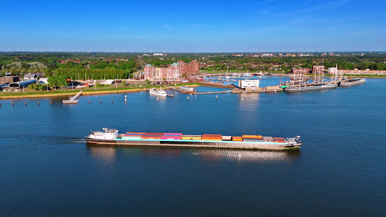 Barge loaded with containers by the beautiful blue waterscape. Port of Lelystad, the Netherlands and green cityscape at backdrop. Aerial view.