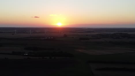 drone flies to sunset, with lush green farm landscape on the ground, in snedsted