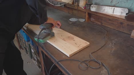 Lower-body-closeup-of-man-renewing-wooden-plank-with-power-sander,-interior-view